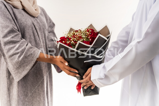 انتقاء باقة مميزة من الورود، تقديم الزهور في الأعياد والمناسبات السعيدة، حفلة ذكرى الزواج، زوجان سعيدان يحتفلان بعيد الحب , بورتريه مقرب لرجل عربي خليجي عماني يرتدي الدشداشة و الكمة يقدم لزوجته باقة من الورد الاحمر، خلفية بيضاء