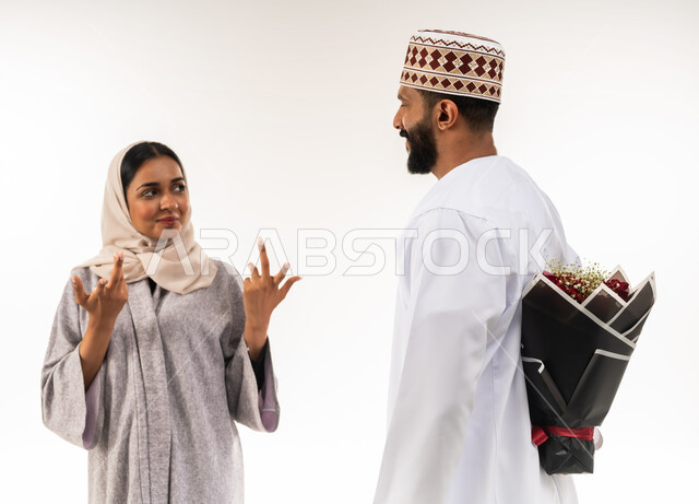 تبادل المودة بين أفراد الأسرة، حفلة ذكرى الزواج، زوجان سعيدان يحتفلان بعيد الحب , بورتريه مقرب لرجل عربي خليجي عماني يرتدي الدشداشة و الكمة يقدم لزوجته باقة من الورد الاحمر، إيماءات الدهشة والفرح، الاحتفال بالمناسبات الرومنسية، خلفية بيضاء