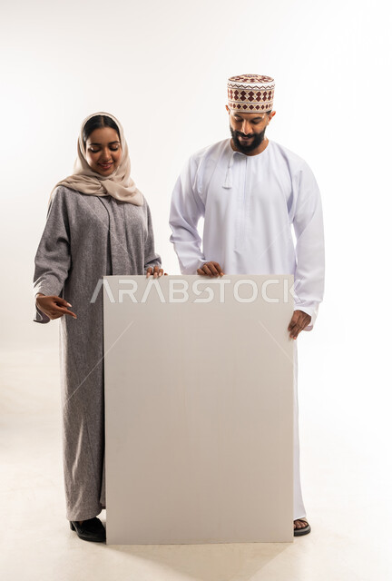 موك اب فارغ، الاعلانات والعروض التسويقية، استخدام لوحات توضيحية ووسائل تعليمية، بورتريه لرجل عربي خليجي عماني مبتسم يرتدي الدشداشه والكمه يقف مع زوجته وبجانبهم لوح ابيض كبير، الجسم بالطول الكامل، خلفية بيضاء