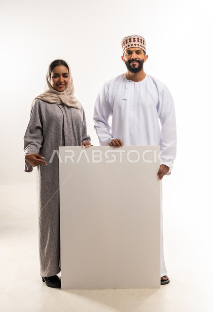 موك اب فارغ، الاعلانات والعروض التسويقية، استخدام لوحات توضيحية ووسائل تعليمية، بورتريه لرجل عربي خليجي عماني مبتسم يرتدي الدشداشه والكمه يقف مع زوجته وبجانبهم لوح ابيض كبير، الجسم بالطول الكامل، خلفية بيضاء