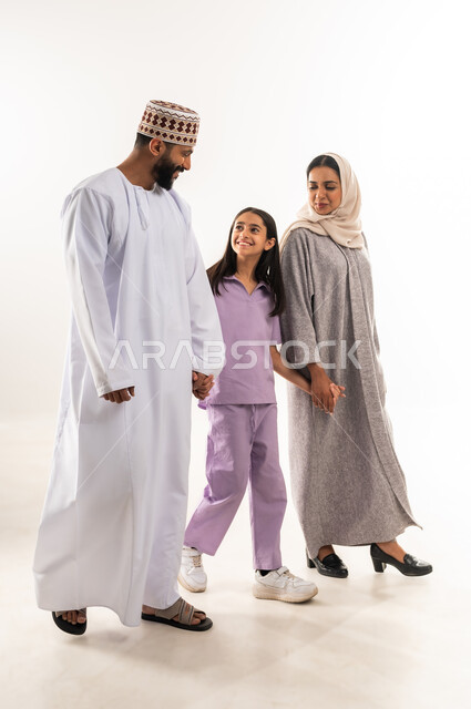 الرعايه والاهتمام بالأبناء, تبادل الحوارات والنقاشات المسلية، عائلة عمانية تقضي اوقات ممتعة،  بورتريه لرجل عربي خليجي عماني يرتدي الدشداشة والكمة يقف مع زوجته وابنته بايماءات السعادة والسرور، تعزيز العلاقات الاجتماعية، الجسم بالطول الكامل، خلفية بيضاء