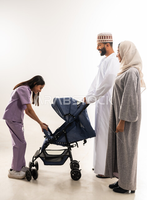 Caring for and paying attention to children, the importance of parents and their primary role in raising and educating children, a portrait of an Arab Gulf Omani man wearing a dishdasha and a kummah standing with his wife and daughter and pulling a baby carriage, going on family outings and tours, an Omani family spending enjoyable times, white background