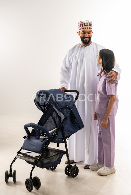 Caring for and paying attention to children, the importance of the father and his essential role in raising and educating children, a portrait of an Arab Gulf Omani man wearing a dishdasha and a kummah pulling a baby carriage with his daughter, going on family outings and tours, an Omani family spending fun and entertaining times, white background