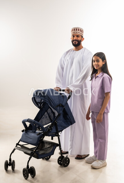 أهمية الأب ودوره الأساسي في تربية ونشأة الأبناء, الرعايه والاهتمام بالأولاد، بورتريه لرجل عربي خليجي عماني يرتدي الدشداسة والكمة يقوم بجرعربة الأطفال مع ابنته, القيام بالنزهات والجولات العائلية، عائلة عمانية تقضي اوقات ممتعة ومسلية، خلفية بيضاء