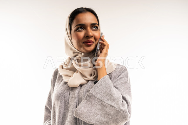 قضاء اوقات ممتعة بتبادل الاخبار والأحاديث، الإجابة والرد على الاتصالات بإستخدام الهاتف المحمول، بورتريه مقرب لامرأة عربية  خليجية عمانية ترتدي عباءة ملونة تنظر الى مكان ما، شابة سعودية تقوم بإجراء مكالمة صوتية عبر الجوال، التواصل والاطمئنان على الأصدقاء، خلفية بيضاء