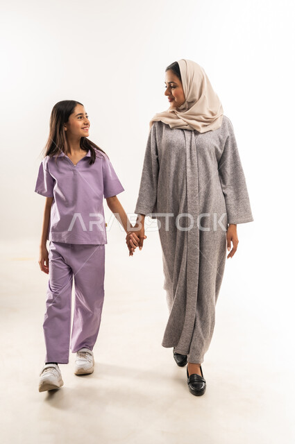 تبادل الحوارات والنقاشات المسلية، عائلة عمانية تقضي اوقات ممتعة، بورتريه لامرأة عربية خليجية سعودية محجبة ترتدي عباءة ملونة تمسك بيد ابنتها بايماءات السعادة والسرور، تعزيز العلاقات الاجتماعية، الجسم بالطول الكامل، خلفية بيضاء