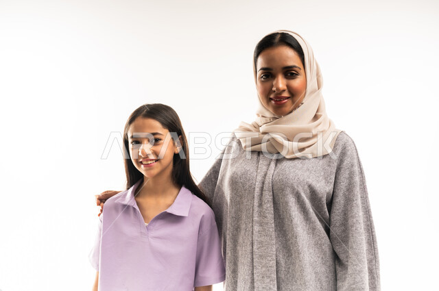 عائلة عمانية تقضي اوقات ممتعة، النظر الى الكاميرا بايماءات السعادة والسرور، بورتريه مقرب لامرأة عربية خليجية سعودية محجبة ترتدي عباءة ملونة تقف مع ابنتها، تبادل الحوارات والنقاشات المسلية، تعزيز العلاقات الاجتماعية، خلفية بيضاء