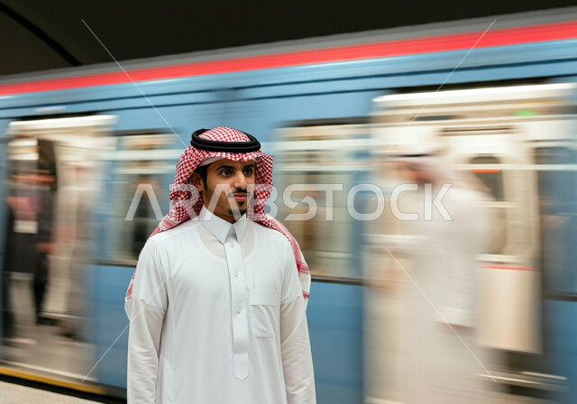 مفهوم التنقل السريع والآمن في السعودية, الاستعداد لركوب القطار, توفير وتسهيل خدمات النقل الحديثة, تطور وتقدم وسائل المواصلات في المملكة, رجل عربي خليجي سعودي يرتدي الثوب التقليدي والشماغ يقف في محطة مترو الرياض