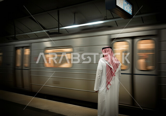 توفير وتسهيل خدمات النقل الحديثة, تطور وتقدم وسائل المواصلات في المملكة, صورة من الخلف لرجل عربي خليجي سعودي يرتدي الثوب التقليدي والشماغ يقف في محطة مترو الرياض, مفهوم التنقل السريع والآمن في السعودية, الاستعداد لركوب القطار