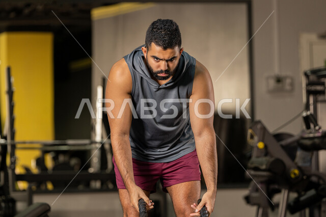 تعابير القوة والعزم، أسلوب حياة صحي، مفهوم الرشاقة واللياقة البدنية، المحافظة على توازن الجسم، انشطة ورياضات لتقوية العضلات والاعصاب، رجل عربي خليجي اماراتي يرتدي الملابس الرياضية يقوم بممارسة التمارين بواسطة الحبل الثقيل، شاب سعودي يتمرن داخل النادي الرياضي