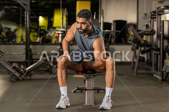 إيماءات القوة والعزم، الاهتمام بالصحة واللياقة الجسدية، رياضة كمال الأجسام، استخدام الاثقال الرياضية، شاب عربي خليجي اماراتي يرتدي الزي الرياضي يقوم بممارسة تمارين رفع الأوزان، رجل سعودي يحمل بيده الدامبلز، بناء الكتلة العضلية للجسم