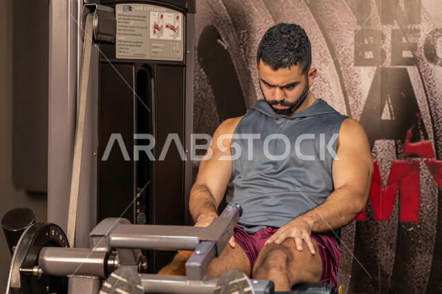 بناء الكتلة العضلية، تقوية العضلات والاعصاب، مفهوم الرشاقة واللياقة البدنية، رجل عربي خليجي إماراتي يرتدي الملابس الرياضية يتمرن على جهاز تمارين الارجل في الجيم، أسلوب حياة صحي، المحافظة على توازن الجسم، شاب سعودي يتدرب داخل النادي
