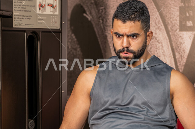 النظر والتركيز في شيء ما، مفهوم الرشاقة واللياقة البدنية, رجل عربي خليجي إماراتي يرتدي الملابس الرياضية يقوم بممارسة التمارين في الجيم, أسلوب حياة صحي، تقوية الأعصاب والعضلات، المحافظة على توازن الجسم، شاب سعودي يتمرن داخل النادي الرياضي