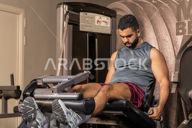 Strengthening muscles and nerves, building muscle mass, the concept of fitness and agility, an Arab Gulf Emirati man wearing sportswear exercising on a leg exercise machine in the gym, a healthy lifestyle, maintaining body balance, a Saudi young man training inside the club