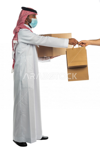 Portrait of a Saudi Arabian Gulf man working in the delivery of orders and goods to customers, online shopping, online orders, smart shopping, reliable shipping and delivery process, delivery representative, commitment to preventive precautions, express d