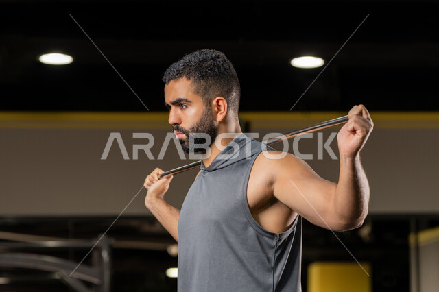 Importance of sports to build a strong body, increase flexibility and stretch muscles, maintain physical fitness, close-up side view of a Saudi man doing an exercise to improve posture and balance, young Arab Gulf Emirati man wearing sportswear exercises with a rubber resistance band, healthy lifestyle