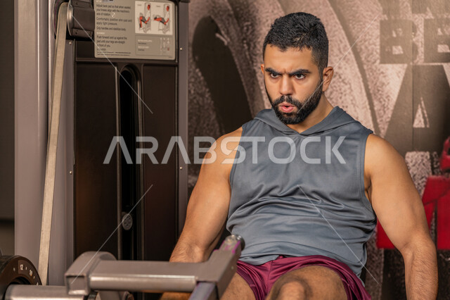 تقوية العضلات والاعصاب، بناء الكتلة العضلية، مفهوم الرشاقة واللياقة البدنية، رجل عربي خليجي إماراتي يرتدي الملابس الرياضية يتمرن على جهاز تمارين الارجل في الجيم، أسلوب حياة صحي، المحافظة على توازن الجسم، شاب سعودي يتدرب داخل النادي