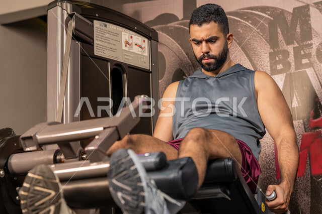 تقوية العضلات والاعصاب، بناء الكتلة العضلية، مفهوم الرشاقة واللياقة البدنية، رجل عربي خليجي إماراتي يرتدي الملابس الرياضية يتمرن على جهاز تمارين الارجل في الجيم، أسلوب حياة صحي، المحافظة على توازن الجسم، شاب سعودي يتدرب داخل النادي