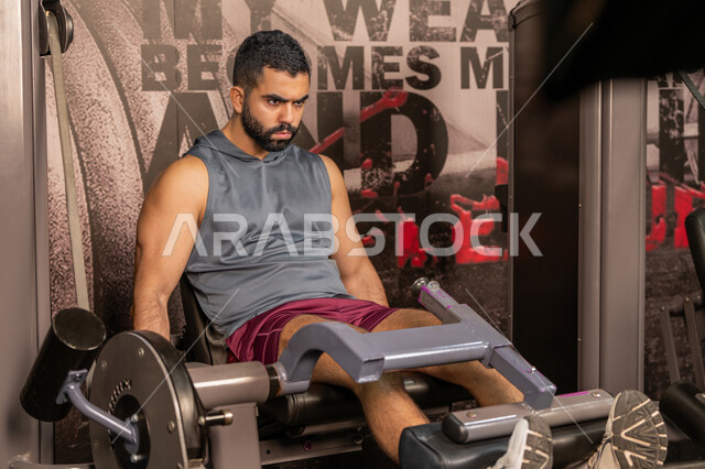 تقوية العضلات والاعصاب، بناء الكتلة العضلية، مفهوم الرشاقة واللياقة البدنية، رجل عربي خليجي إماراتي يرتدي الملابس الرياضية يتمرن على جهاز تمارين الارجل في الجيم، أسلوب حياة صحي، المحافظة على توازن الجسم، شاب سعودي يتدرب داخل النادي