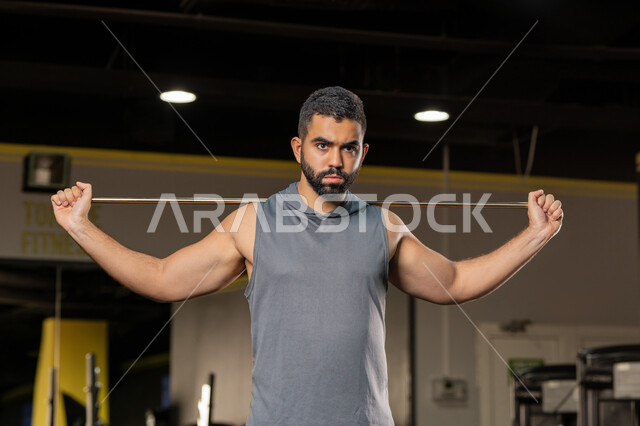 ايماءات القوة والعزم، أسلوب حياة صحي، المحافظة على اللياقة البدنية، أهمية الرياضة لبناء جسد قوي، زيادة المرونة وتمديد العضلات، صورة مقربة لرجل سعودي يمارس تمرين لتحسين وضعية الجسم والتوازن، شاب عربي خليجي اماراتي يرتدي الملابس الرياضية يتمرن حبل المقاومة المطاطي