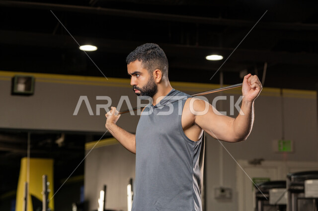 Muscle stretching and flexibility, healthy lifestyle, maintaining fitness, importance of sports to build a strong body, close-up side view of a Saudi man doing an exercise to improve posture and balance, young Arab Gulf Emirati man wearing sportswear exercises with a rubber resistance band