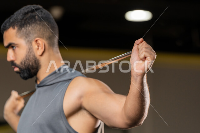 Importance of sports to build a strong body, increase flexibility and stretch muscles, maintain physical fitness, close-up side view of a Saudi man doing an exercise to improve posture and balance, young Arab Gulf Emirati man wearing sportswear exercises with a rubber resistance band, healthy lifestyle