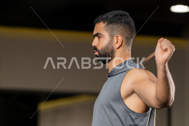 Increase flexibility and stretch muscles, youth activity that helps with physical fitness, importance of sports to build a strong body, Saudi man doing exercise to improve posture and balance, young Arab Gulf Emirati man wearing sportswear exercises with a stick, healthy lifestyle, expressions of strength and determination