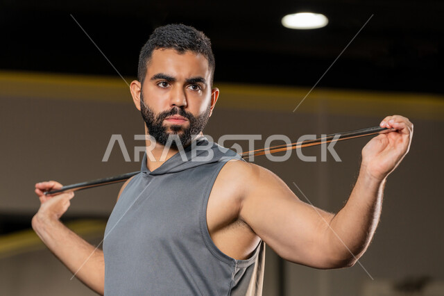 Expressions of strength and determination, increasing flexibility and stretching muscles, youth activity that helps with physical fitness, importance of sports to build a strong body, Saudi man doing an exercise to improve posture and balance, young Arab Gulf Emirati man wearing sportswear exercises using a stick, healthy lifestyle