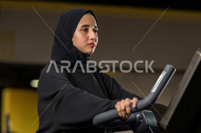 إنقاص الوزن وحرق السعرات الحرارية، نشاط شبابي يساعد على اللياقة البدنية, أهمية الرياضة لبناء جسد قوي، امراة سعودية تمارس تمرين لتحسين وضعية الجسم والتوازن، شابة عربية خليجية إماراتية محجبة ترتدي الزي الرياضي تقوم بممارسة التمارين على جهاز التجذيف