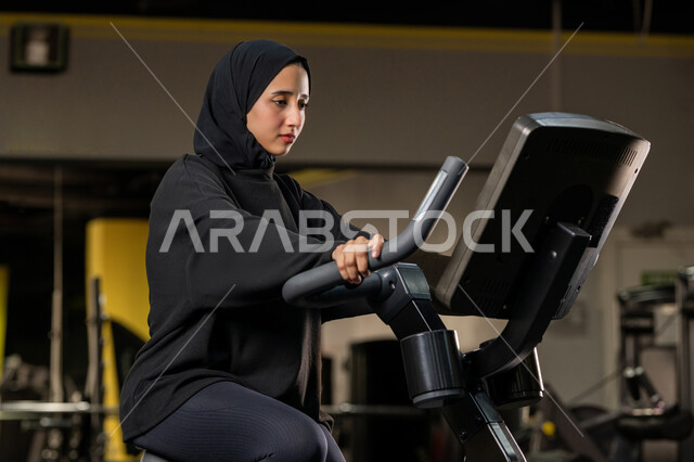 نشاط شبابي يساعد على اللياقة البدنية, أهمية الرياضة لبناء جسد قوي، حرق السعرات الحرارية وإنقاص الوزن، امراة سعودية تمارس تمرين لتحسين وضعية الجسم والتوازن، شابة عربية خليجية إماراتية محجبة ترتدي الزي الرياضي تقوم بممارسة التمارين على جهاز التجذيف
