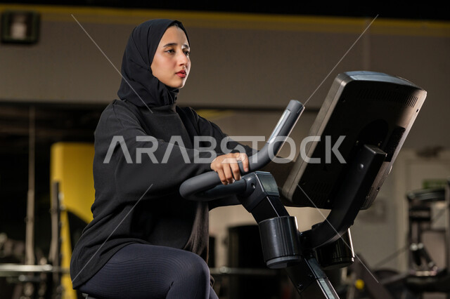 نشاط شبابي يساعد على اللياقة البدنية, أهمية الرياضة لبناء جسد قوي، حرق السعرات الحرارية وإنقاص الوزن، امراة سعودية تمارس تمرين لتحسين وضعية الجسم والتوازن، شابة عربية خليجية إماراتية محجبة ترتدي الزي الرياضي تقوم بممارسة التمارين على جهاز التجذيف