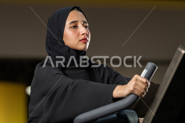إنقاص الوزن وحرق السعرات الحرارية، نشاط شبابي يساعد على اللياقة البدنية, أهمية الرياضة لبناء جسد قوي، امراة سعودية تمارس تمرين لتحسين وضعية الجسم والتوازن، شابة عربية خليجية إماراتية محجبة ترتدي الزي الرياضي تقوم بممارسة التمارين على جهاز التجذيف