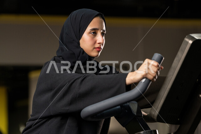 شابة عربية خليجية إماراتية محجبة ترتدي الزي الرياضي تقوم بممارسة التمارين على جهاز التجذيف، نشاط شبابي يساعد على اللياقة البدنية, أهمية الرياضة لبناء جسد قوي، حرق السعرات الحرارية وإنقاص الوزن، امراة سعودية تمارس تمرين لتحسين وضعية الجسم والتوازن