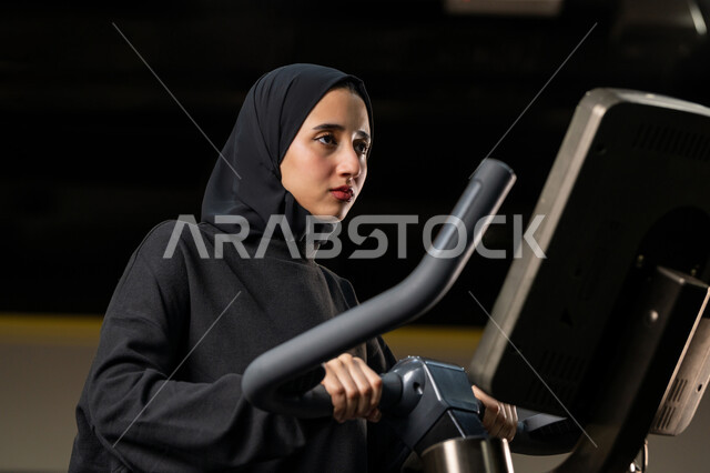 شابة عربية خليجية إماراتية محجبة ترتدي الزي الرياضي تقوم بممارسة التمارين على جهاز التجذيف، نشاط شبابي يساعد على اللياقة البدنية, أهمية الرياضة لبناء جسد قوي، حرق السعرات الحرارية وإنقاص الوزن، امراة سعودية تمارس تمرين لتحسين وضعية الجسم والتوازن