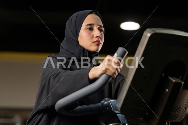 نشاط شبابي يساعد على اللياقة البدنية, أهمية الرياضة لبناء جسد قوي، حرق السعرات الحرارية وإنقاص الوزن، امراة سعودية تمارس تمرين لتحسين وضعية الجسم والتوازن، شابة عربية خليجية إماراتية محجبة ترتدي الزي الرياضي تقوم بممارسة التمارين على جهاز التجذيف