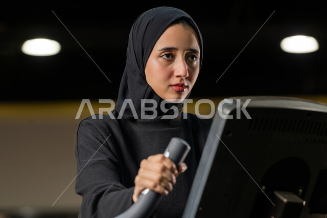 إنقاص الوزن وحرق السعرات الحرارية، نشاط شبابي يساعد على اللياقة البدنية, أهمية الرياضة لبناء جسد قوي، امراة سعودية تمارس تمرين لتحسين وضعية الجسم والتوازن، شابة عربية خليجية إماراتية محجبة ترتدي الزي الرياضي تقوم بممارسة التمارين على جهاز التجذيف