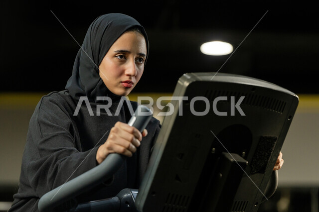 شابة عربية خليجية إماراتية محجبة ترتدي الزي الرياضي تقوم بممارسة التمارين على جهاز التجذيف، نشاط شبابي يساعد على اللياقة البدنية, أهمية الرياضة لبناء جسد قوي، حرق السعرات الحرارية وإنقاص الوزن، امراة سعودية تمارس تمرين لتحسين وضعية الجسم والتوازن