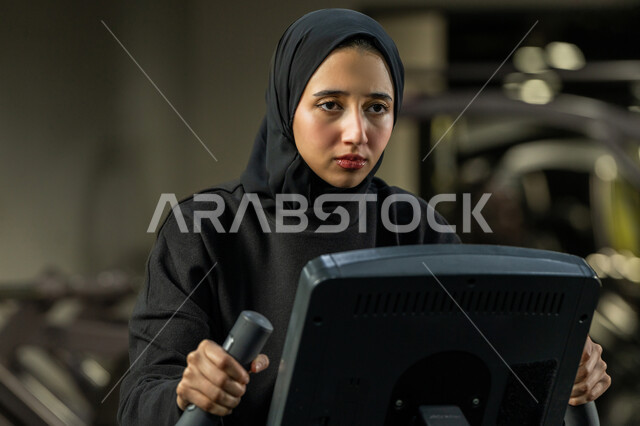 نشاط شبابي يساعد على اللياقة البدنية, أهمية الرياضة لبناء جسد قوي، حرق السعرات الحرارية وإنقاص الوزن، امراة سعودية تمارس تمرين لتحسين وضعية الجسم والتوازن، شابة عربية خليجية إماراتية محجبة ترتدي الزي الرياضي تقوم بممارسة التمارين على جهاز التجذيف