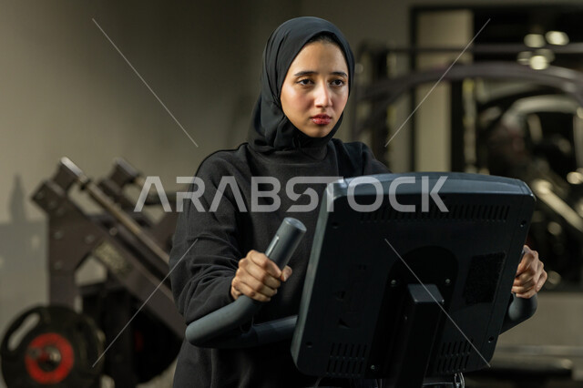 حرق السعرات الحرارية وإنقاص الوزن، نشاط شبابي يساعد على اللياقة البدنية, أهمية الرياضة لبناء جسد قوي، امراة سعودية تمارس تمرين لتحسين وضعية الجسم والتوازن، شابة عربية خليجية إماراتية محجبة ترتدي الزي الرياضي تقوم بممارسة التمارين على جهاز التجذيف
