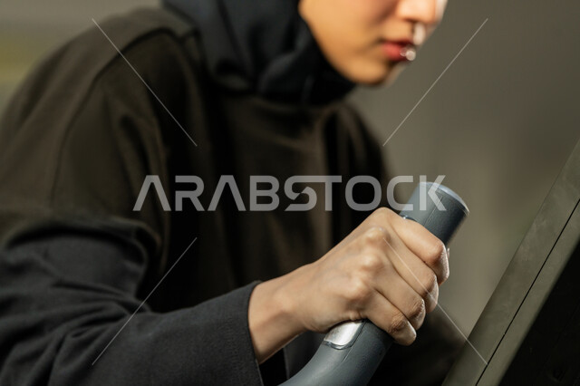 Burn calories and lose weight, youth activity that helps with physical fitness, the importance of sports to build a strong body, a Saudi woman doing an exercise to improve posture and balance, a veiled young Arab Gulf Emirati woman wearing sportswear doing exercises on a rowing machine