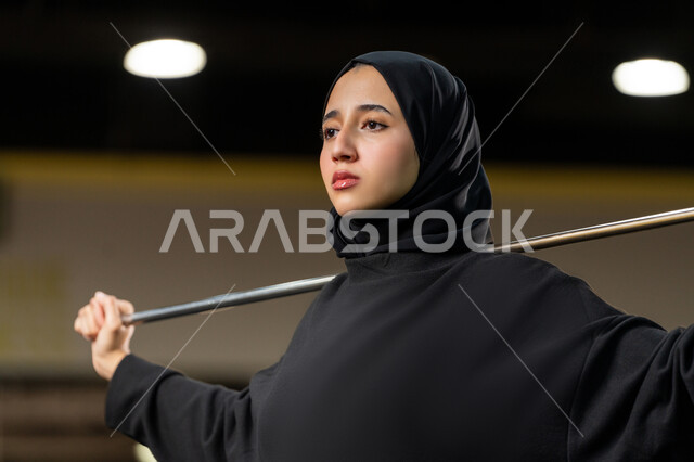 تمديد العضلات وزيادة المرونة، نشاط شبابي يساعد على اللياقة البدنية, أهمية الرياضة لبناء جسد قوي، امراة سعودية تمارس تمرين لتحسين وضعية الجسم والتوازن، شابة عربية خليجية إماراتية محجبة ترتدي الزي الرياضي تتمرن باستخدام العصا، أسلوب حياة صحي