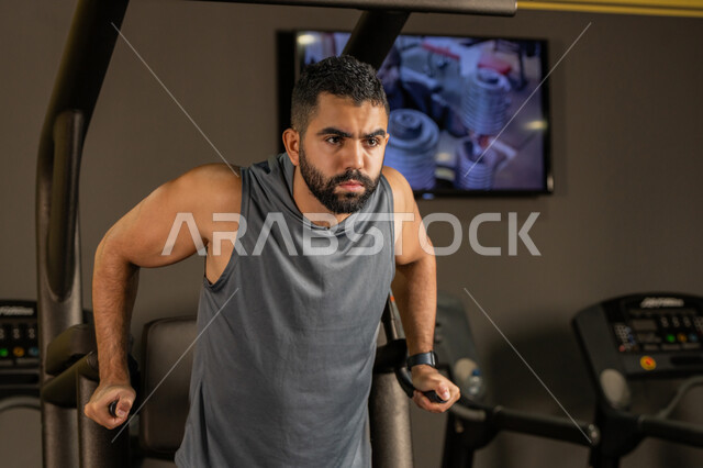نشاط شبابي يساعد على اللياقة البدنية, أهمية الرياضة لبناء جسد قوي، رجل سعودي يمارس تمرين لتقوية عضلات الصدر، رياضة كمال الأجسام، شاب عربي خليجي إماراتي يرتدي الزي الرياضي يقوم بممارسة التمارين على جهاز الغطس المساعد، استخدام الأجهزة الرياضية، أسلوب حياة صحي