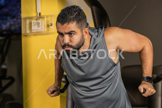 استخدام الأجهزة الرياضية، أسلوب حياة صحي، أهمية الرياضة لبناء جسد قوي، نشاط شبابي يساعد على اللياقة البدنية, رجل سعودي يمارس تمرين لتقوية عضلات الصدر، رياضة كمال الأجسام، شاب عربي خليجي إماراتي يرتدي الزي الرياضي يقوم بممارسة التمارين على جهاز الغطس المساعد