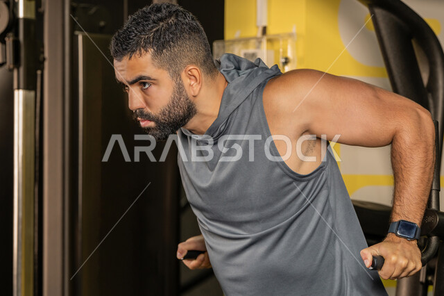 نشاط شبابي يساعد على اللياقة البدنية, أهمية الرياضة لبناء جسد قوي، رجل سعودي يمارس تمرين لتقوية عضلات الصدر، رياضة كمال الأجسام، شاب عربي خليجي إماراتي يرتدي الزي الرياضي يقوم بممارسة التمارين على جهاز الغطس المساعد، استخدام الأجهزة الرياضية، أسلوب حياة صحي