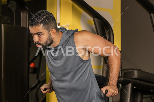 Importance of sports to build a strong body, youth activity that helps with physical fitness, Saudi man doing exercise to strengthen chest muscles, bodybuilding, Emirati Gulf Arab young man wearing sportswear doing exercises on diving aid, using sports equipment, healthy lifestyle