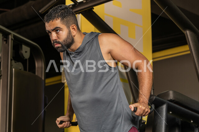 Youth activity that helps with physical fitness, the importance of sports to build a strong body, a Saudi man doing an exercise to strengthen the chest muscles, bodybuilding, a young Arab Gulf Emirati man wearing sportswear doing exercises on the diving aid device, using sports equipment, a healthy lifestyle