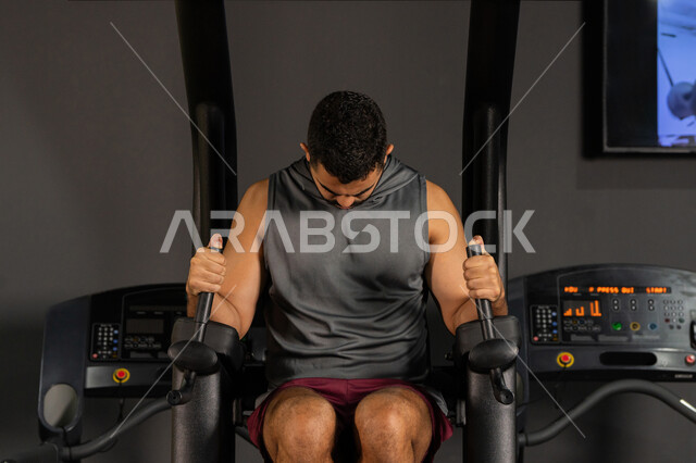 The importance of sports to build a strong body, youth activities that help with physical fitness, a Saudi man doing an exercise to strengthen the chest and shoulder muscles, a healthy lifestyle, bodybuilding, using sports equipment, a young Arab Gulf Emirati man wearing sportswear doing exercises on the parallel bar