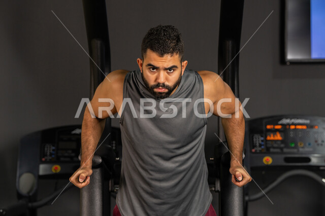 The importance of sports to build a strong body, youth activities that help with physical fitness, a Saudi man doing an exercise to strengthen the chest and shoulder muscles, a healthy lifestyle, bodybuilding, using sports equipment, a young Arab Gulf Emirati man wearing sportswear doing exercises on the parallel bar