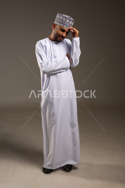 النسيان ومحاولة تذكر شيء ما, الاحساس بالشقيقية والصداع النصفي, الشعور بالإرهاق وفقدان التركيز, بورتريه لرجل عربي خليجي عماني يرتدي الدشداشة والكمة يضع يديه على رأسه ويغمض عينيه بإيماءات وجع في الدماغ والرأس الشديد, الجسم بالطول الكامل, خلفية بيج