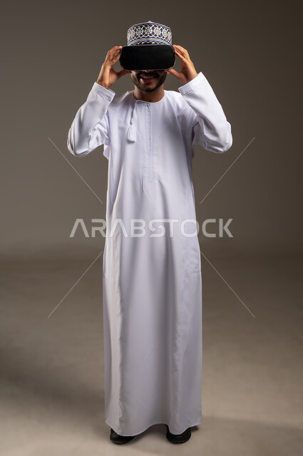 المتعة والتسلية بالمشاهدة عبر نظارة الواقع الافتراضي، بورتريه لشاب عربي خليجي عماني يرتدي الدشداشة والكمة ونظارات ثلاثية الأبعاد (الفي ار), الاندماج ومحاكاة العالم الخيالي، التطور التقني والتكنولوجي, الجسم بالطول الكامل، خلفية بيضاء